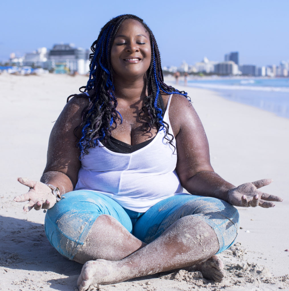 Dianne meditates on the beach, eyes closed, palms turned up to the sun.