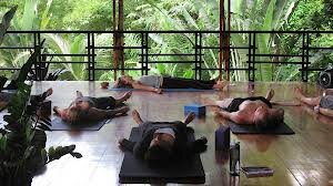 Four yogis lie on the floor in savasana in a tropical location.