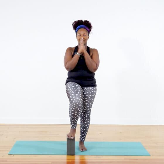 Tree pose variation with foot on block and eyes closed.